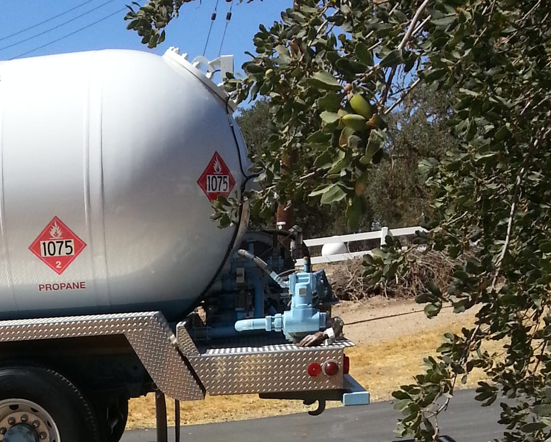 A propane delivery truck at a fill on a rural drive, hose run out to the tank.